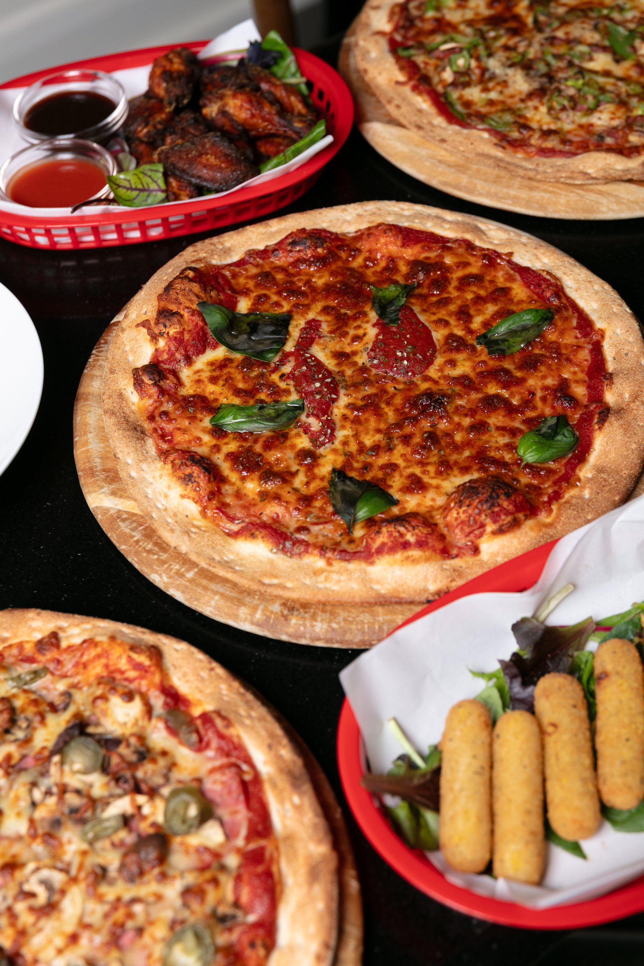 Pizza with fresh basil on a wooden board beside mozzarella sticks
