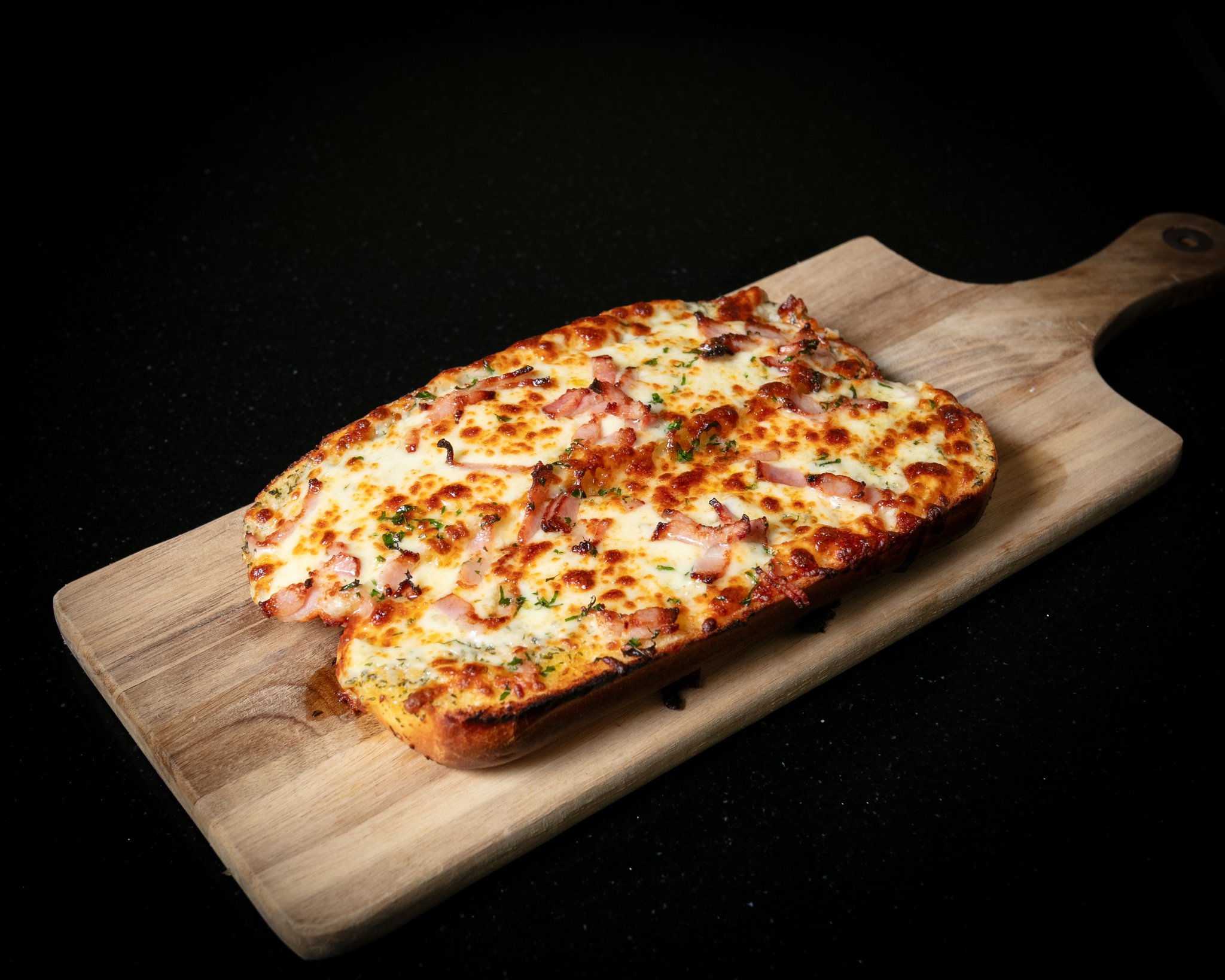 Loaded garlic bread with melted cheese and bacon on a wooden board