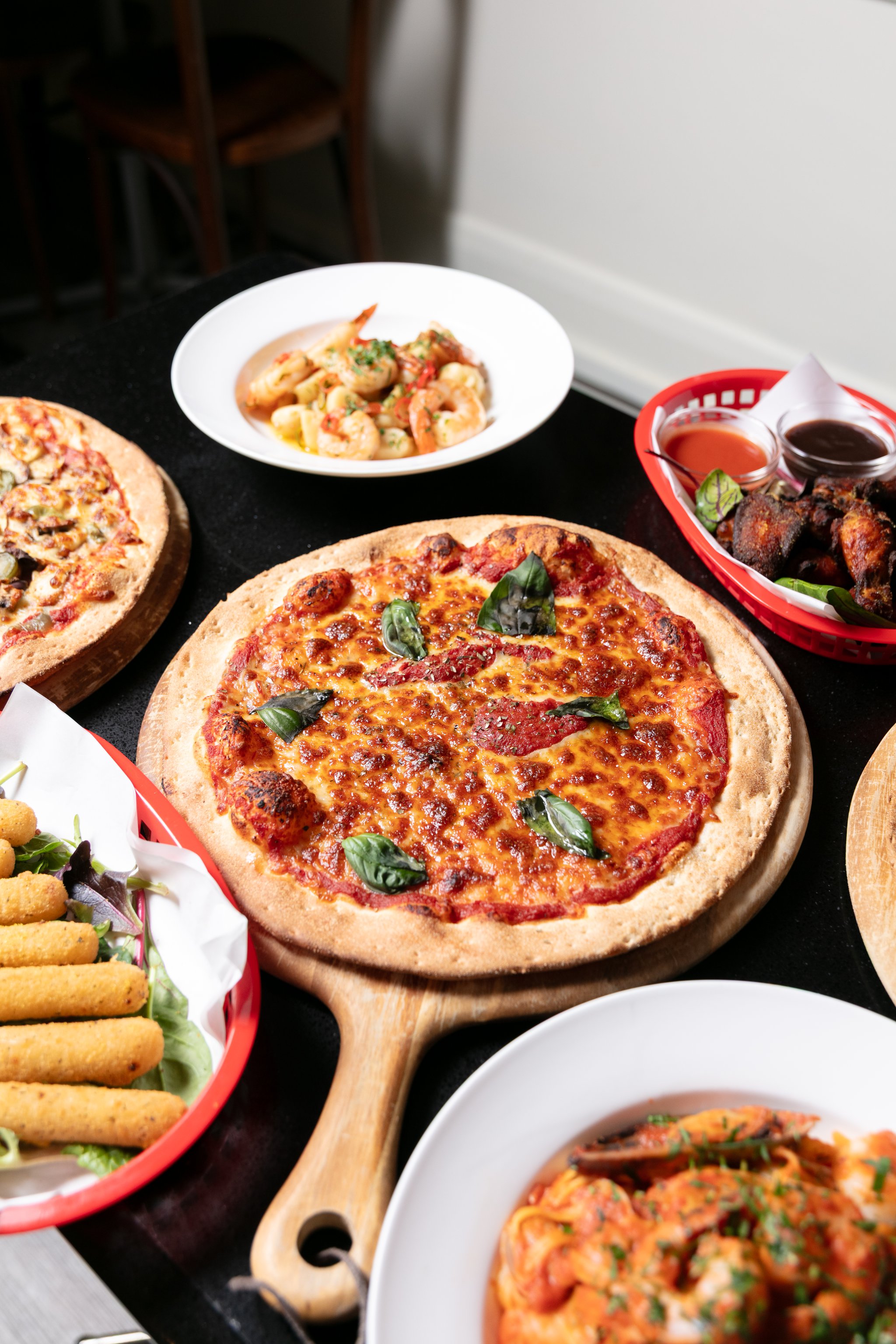 Pizza, garlic prawns and chicken wings served together on a dark table