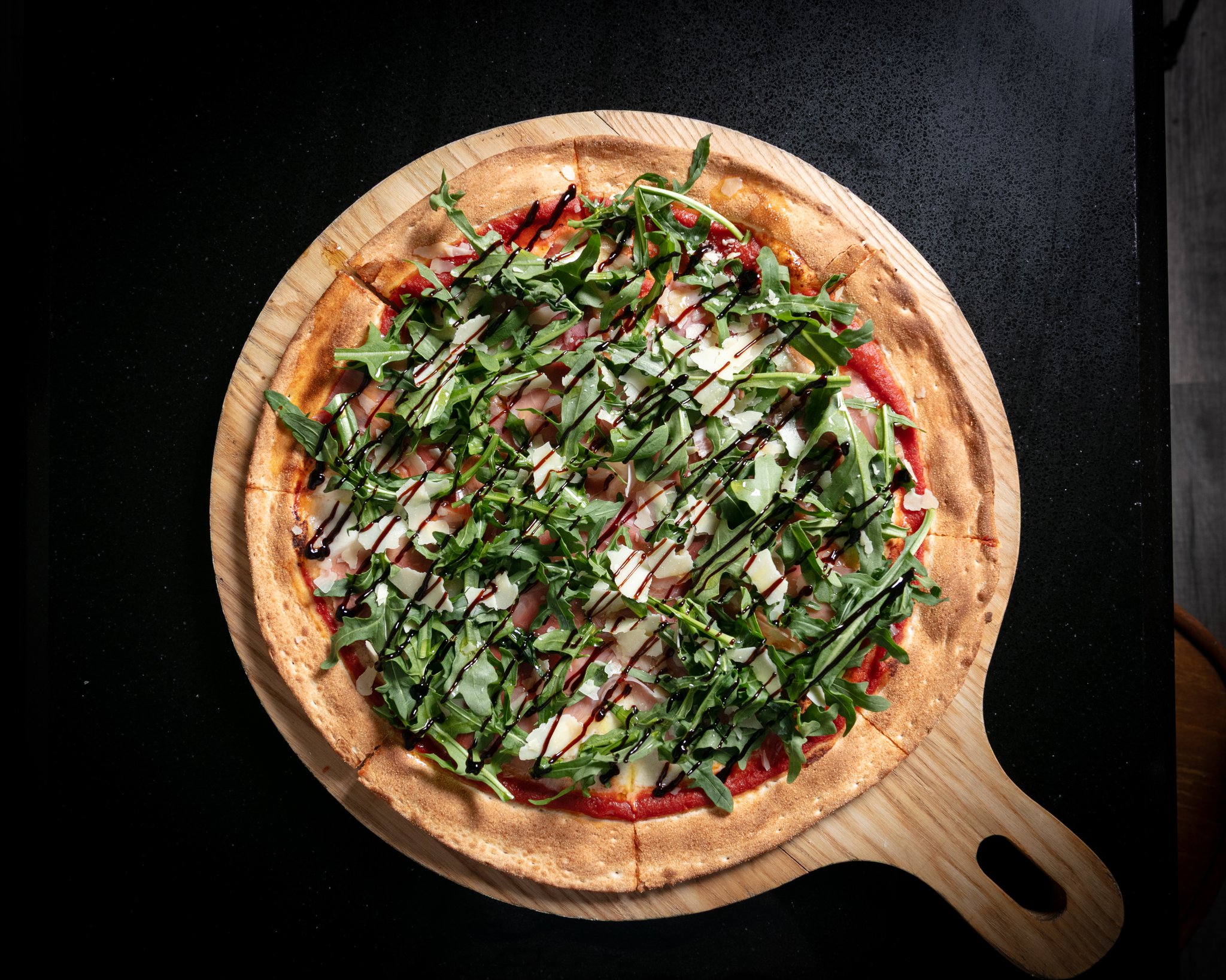 Prosciutto pizza topped with fresh rocket and a drizzle of balsamic glaze