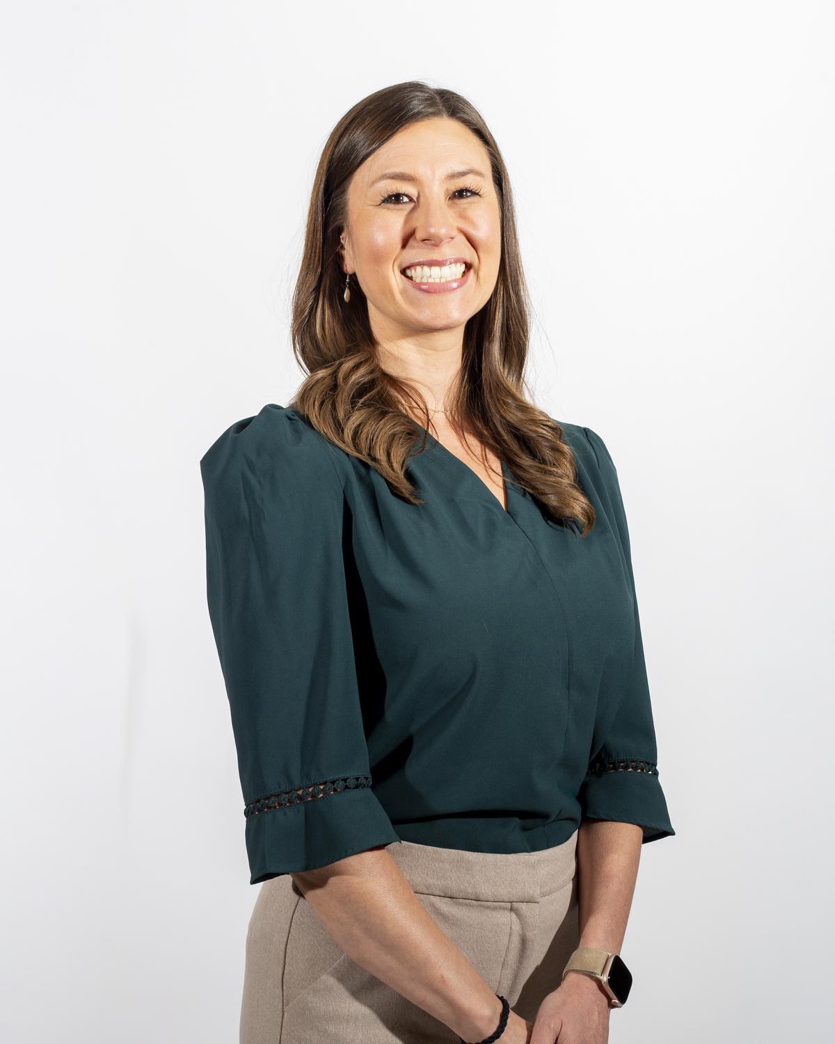 Business portrait of a smiling woman in a green blouse against a white studio backdrop