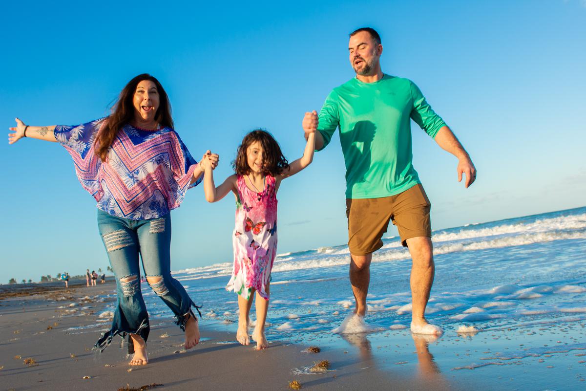 A mother, daughter and father holding hands and running along the beach