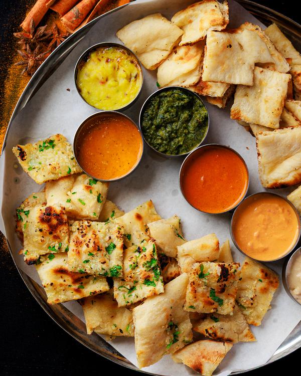 A platter of samosas with four dipping sauces