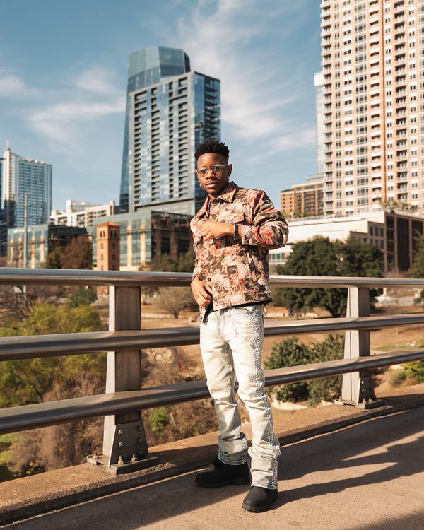 A man in a patterned shirt on a bridge with city towers behind