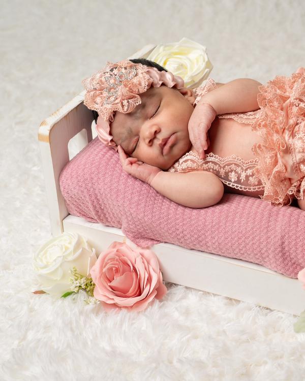 A sleeping newborn in a lace headband on a pink mini bed