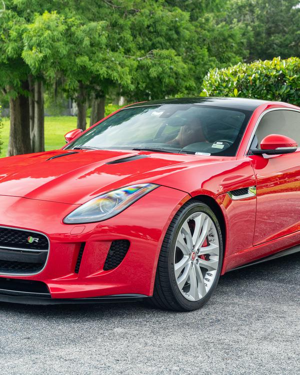 A red sports coupe parked on a driveway in front of green trees