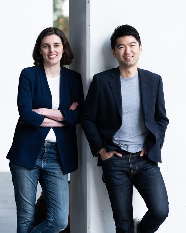 Two colleagues in blazers leaning against a white wall