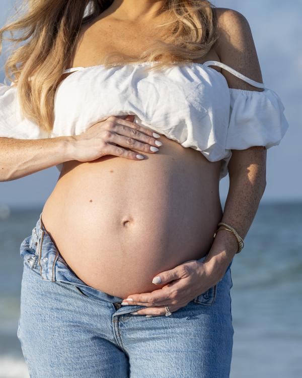 An expectant mother in a white top and jeans holding her bump