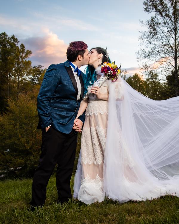 A bride and groom kissing on a lawn, her long veil trailing