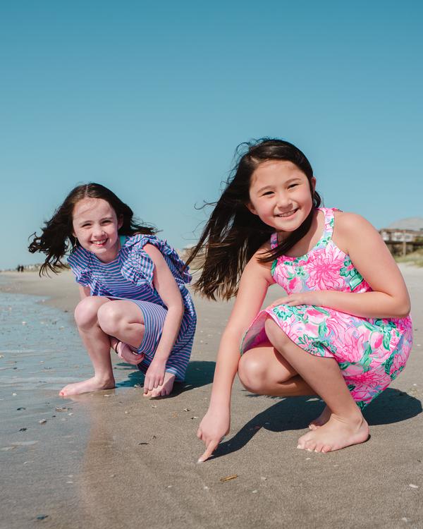 Two girls in summer dresses drawing in the wet sand at the shoreline