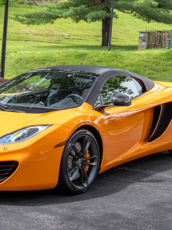 An orange sports car parked on a driveway beside a green lawn