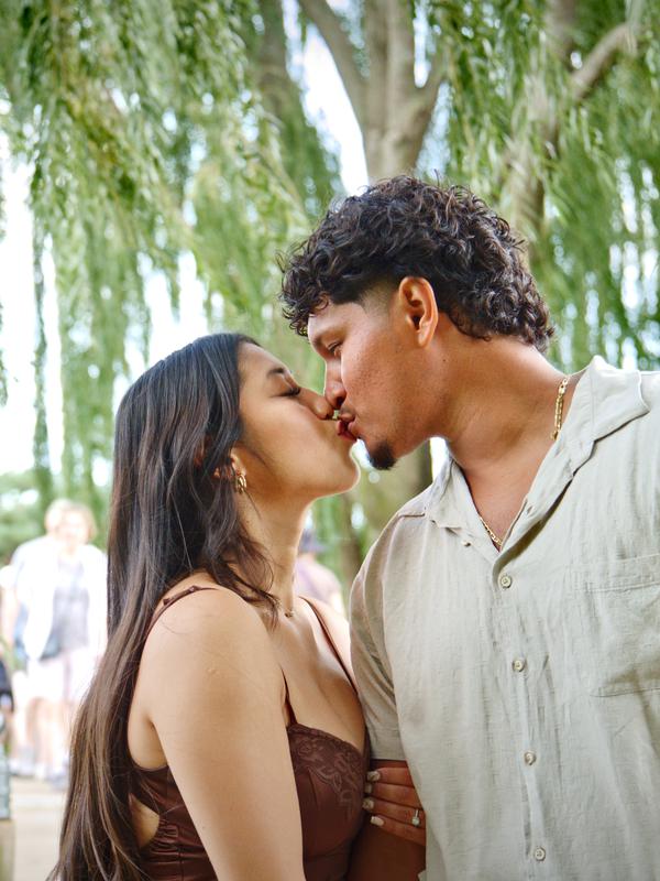 A couple sharing a kiss beneath the branches of a willow tree
