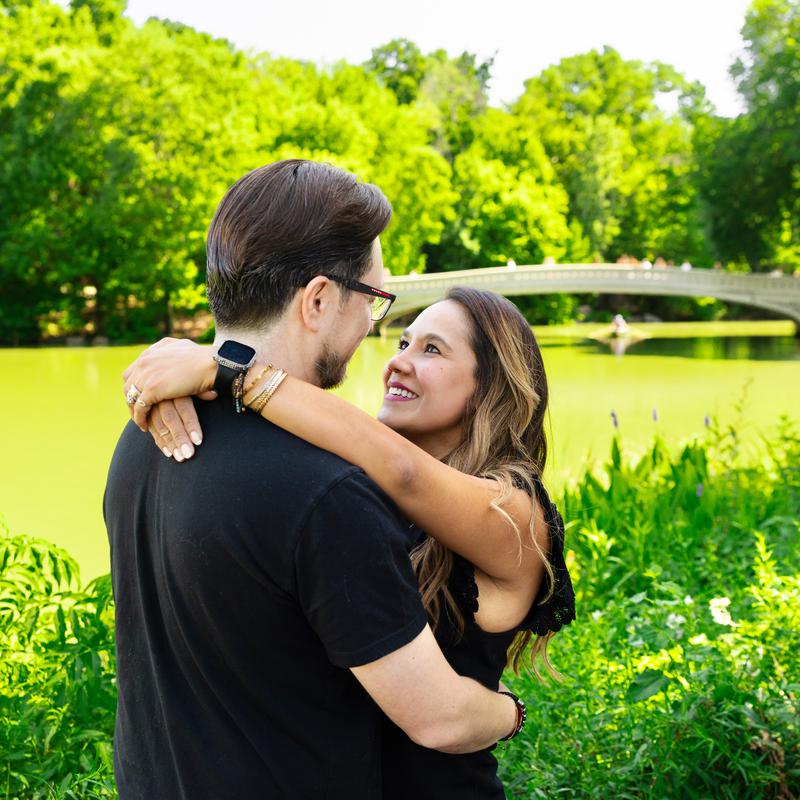 A couple embracing in a green park beside a footbridge