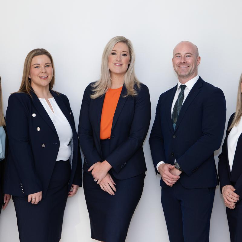 Three colleagues in navy business suits standing together against a white wall
