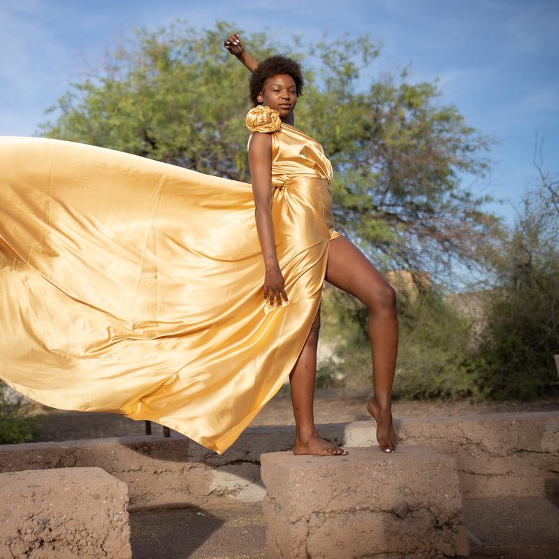 A model in a flowing gold gown posing outdoors on a stone ledge