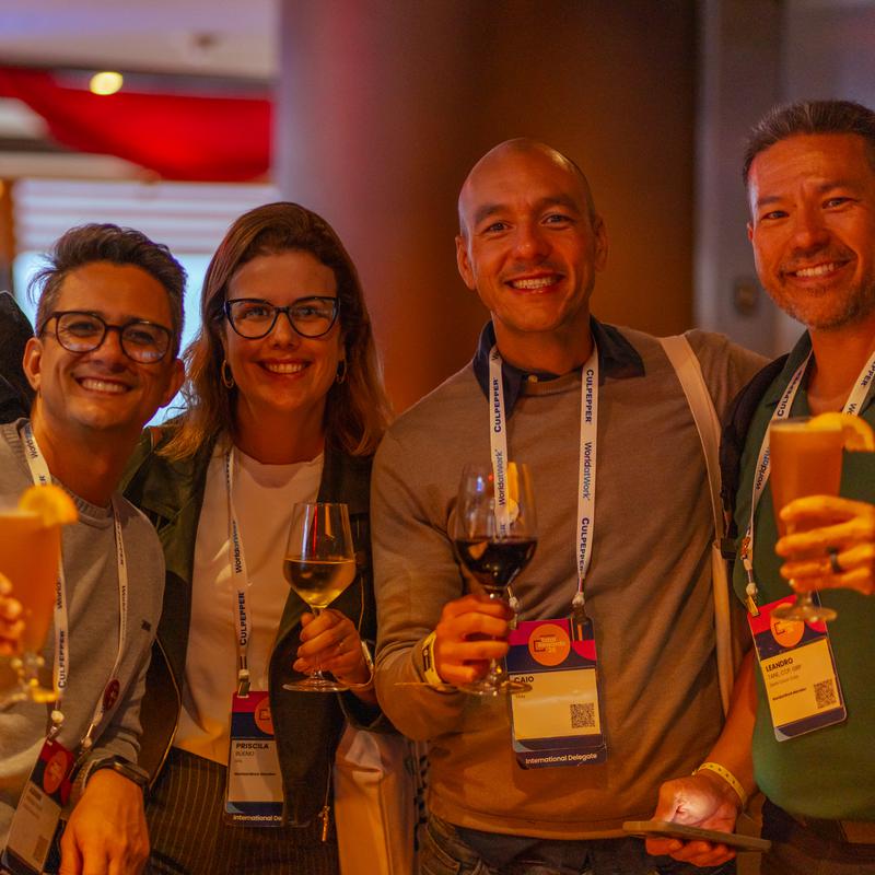 Conference guests wearing lanyards, smiling and raising drinks at an evening reception