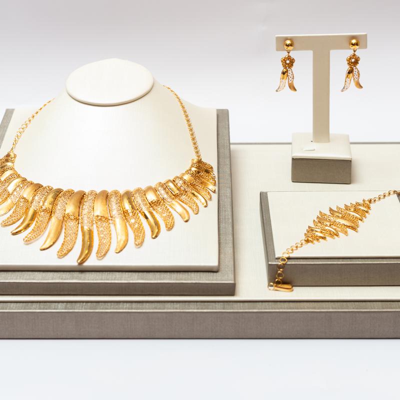 A gold statement necklace, bracelet and earrings on white jewellery display stands