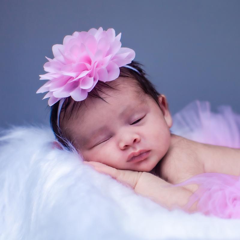 A sleeping newborn in a pink flower headband on a soft white blanket