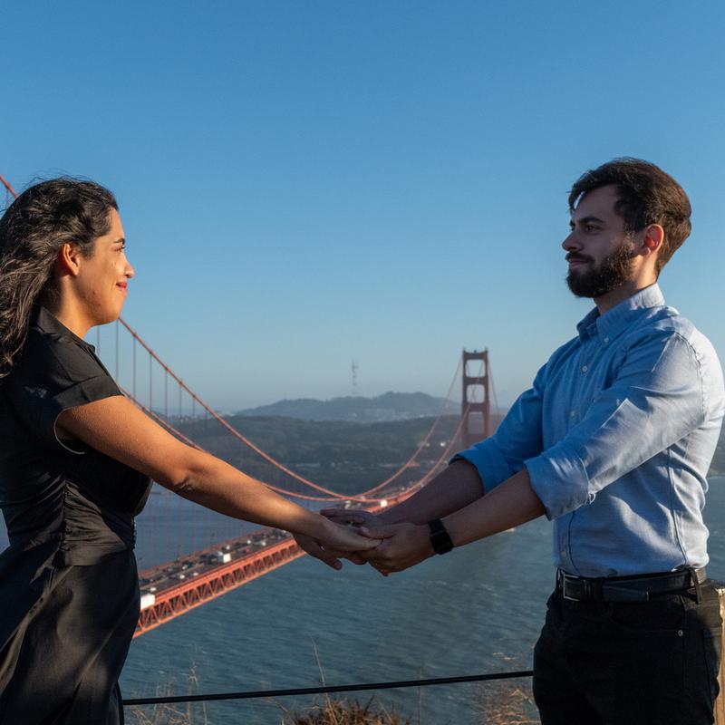 A couple holding hands at a lookout with the Golden Gate Bridge behind them