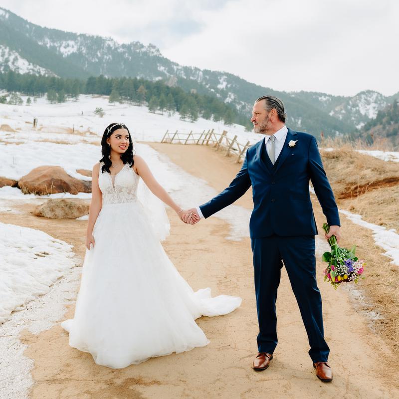 A bride and groom holding hands on a snowy path with mountains behind them