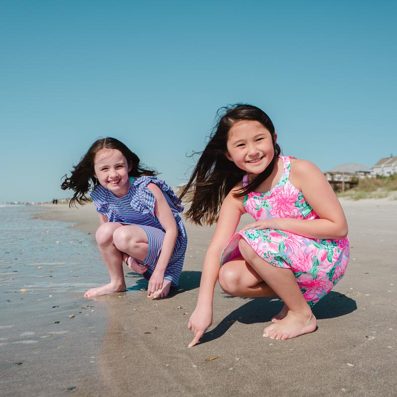 Two young sisters crouching to play in the sand at the beach